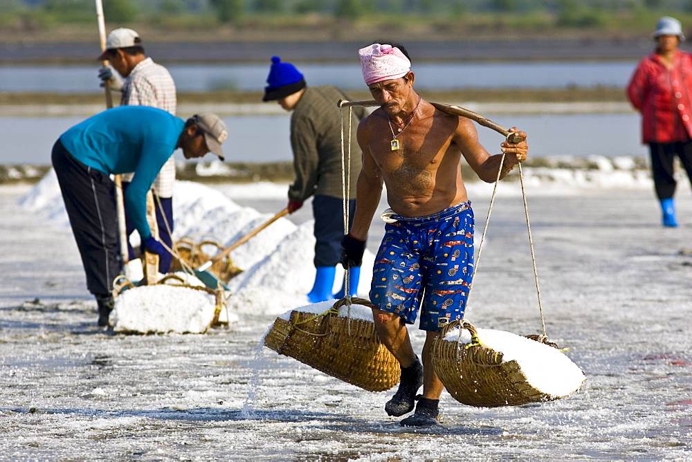 Man carries farmed salt in traditional shoulder baskets, Bangkok, Thailand