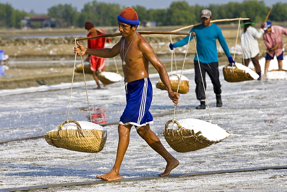 Man carries farmed salt in traditional shoulder baskets, Bangkok, Thailand