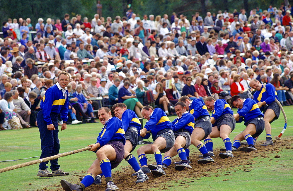 A huge crowd watching a team of men taking part in a tug-of-war competition at the Braemar Games, a Royal Highland gathering.