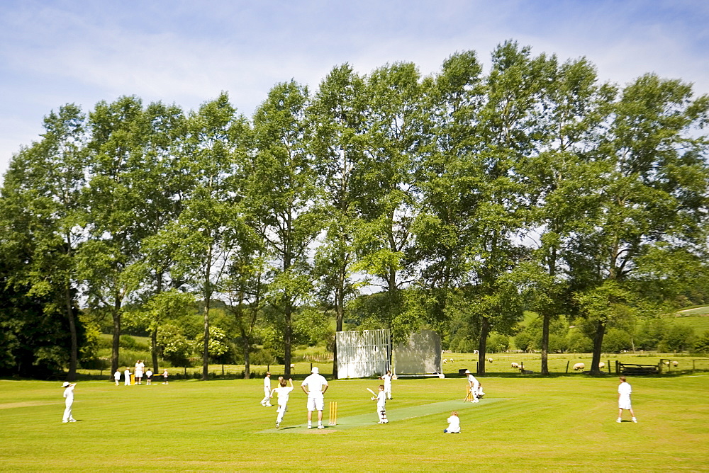 Children play cricket on village pitch, Swinbrook, The Cotswolds, England, United Kingdom