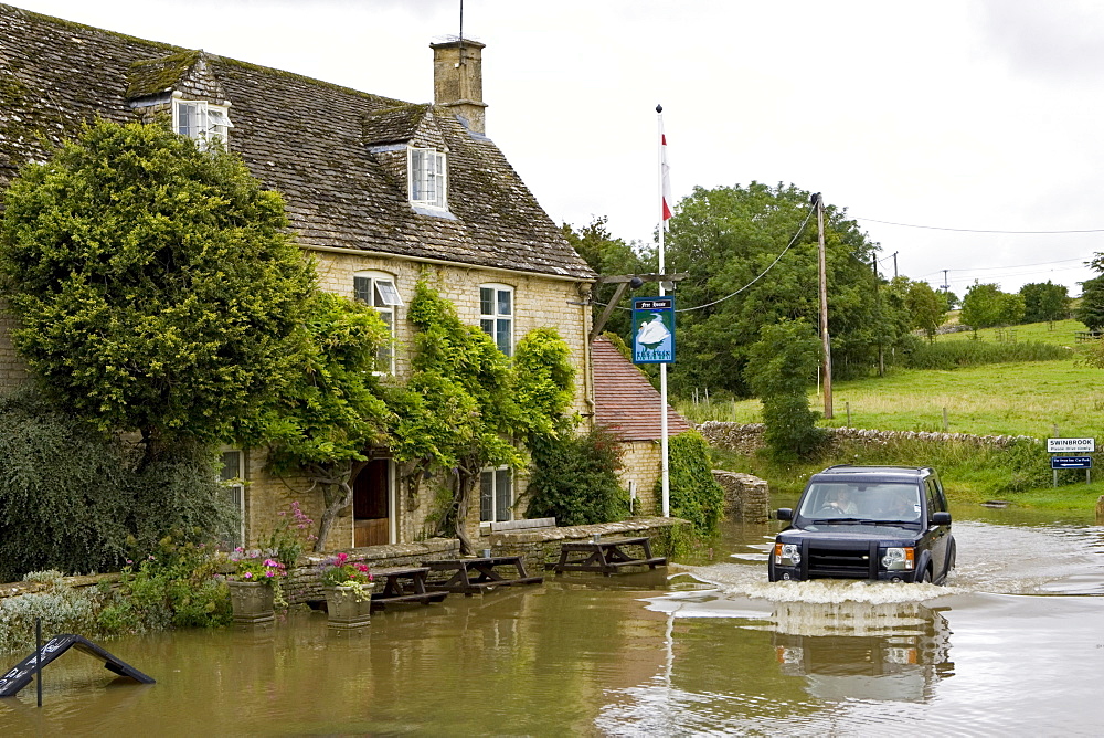 Four wheel drive car drives through flooded road in Swinbrook, Oxfordshire, England, United Kingdom