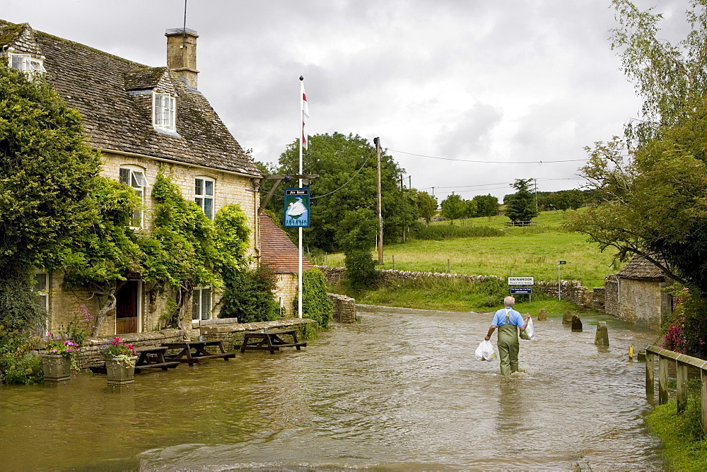 Man wades through flood water in Swinbrook, Oxfordshire, England, United Kingdom