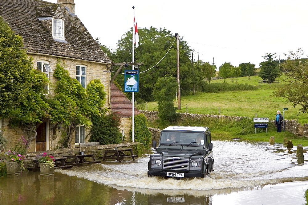 Four wheel drive car drives through flooded road in Swinbrook, Oxfordshire, England, United Kingdom