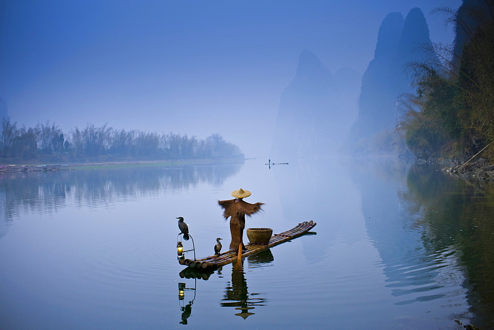 Fisherman in Suoyi coat and coolie hat fishes with cormorants on Li River near Guilin, China