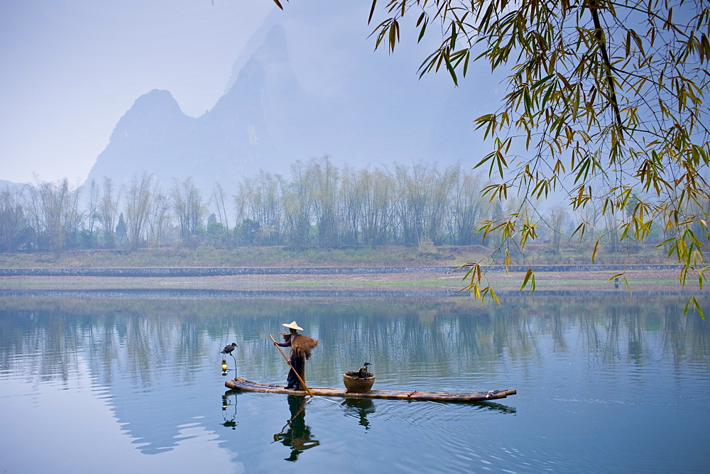 Fisherman in Suoyi coat and coolie hat fishes with cormorants on Li River near Guilin, China