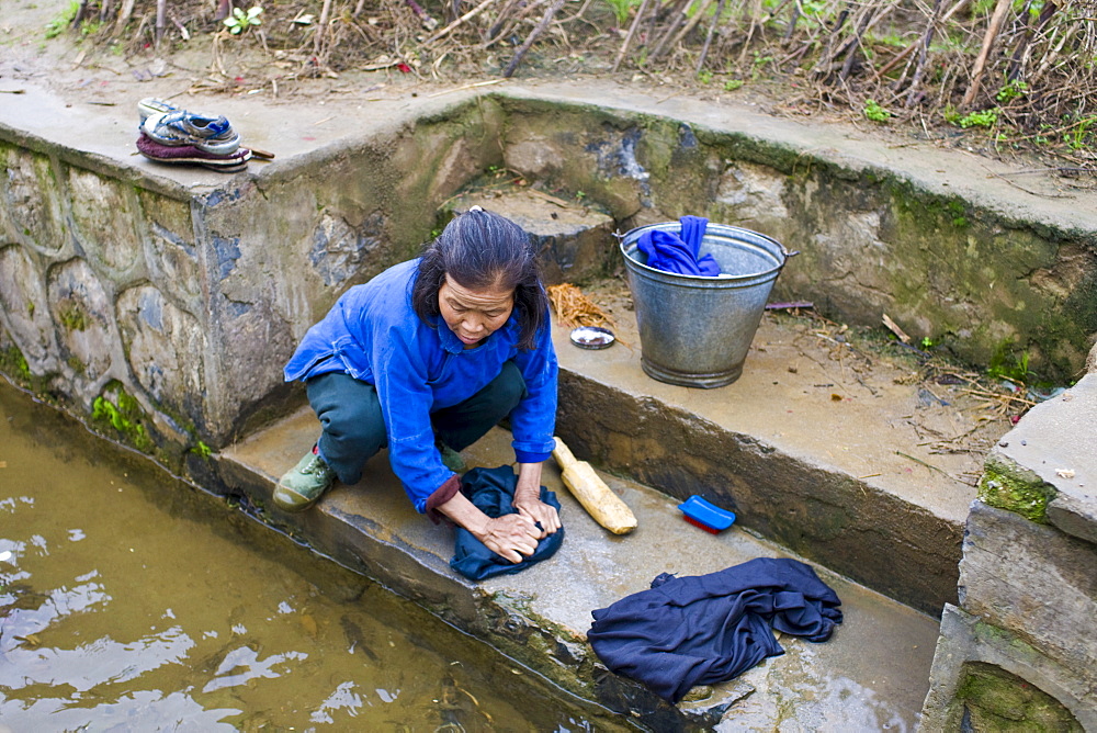 Woman washes her clothes in a stream by the road in Fuli Old Town, Xingping, China