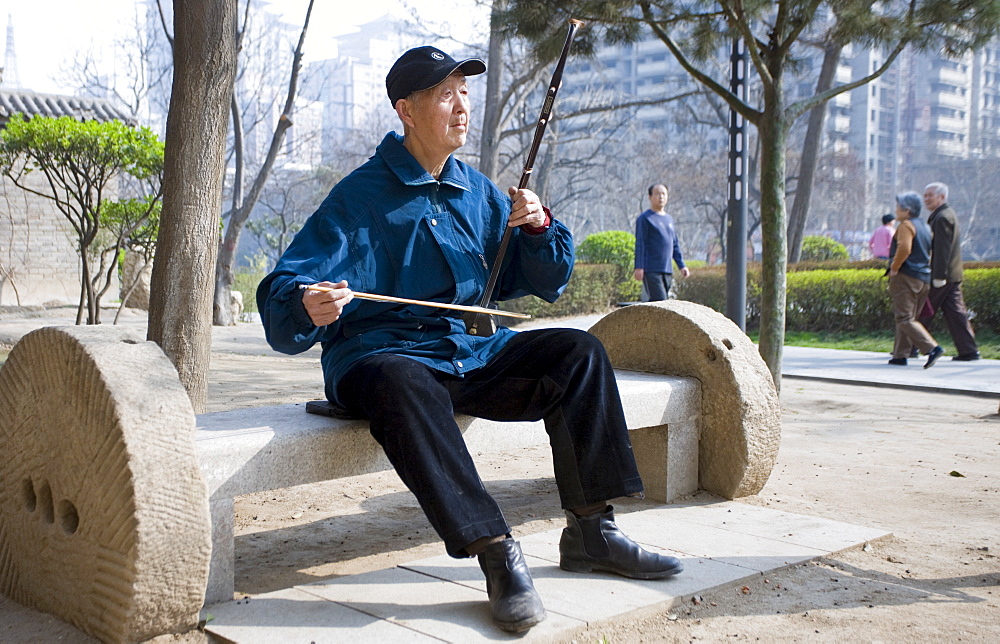 Man plays an Erhu instrument using a bow, in the park by the City Wall, Xian, China