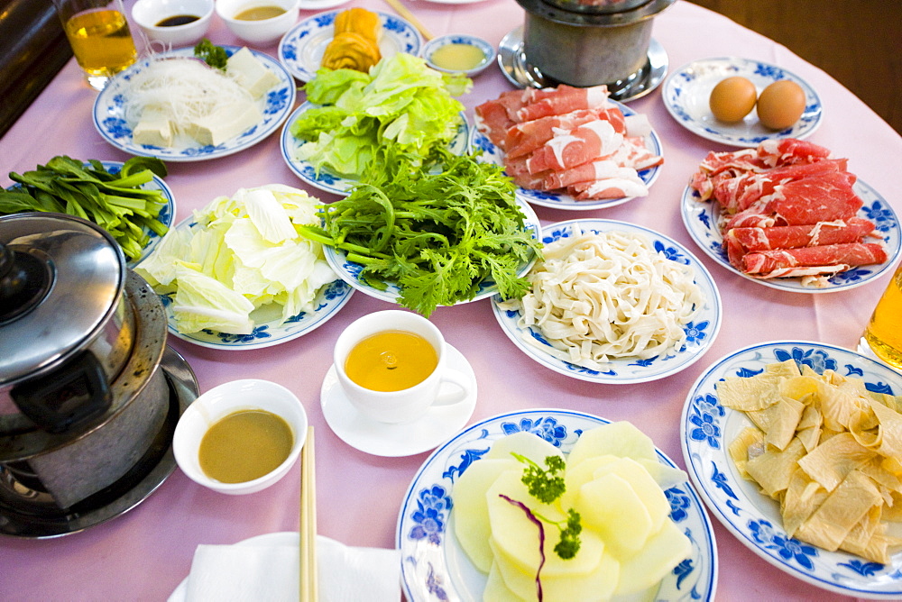 Traditional Chinese Hotpot meal in tourist restaurant, Xian. Diners cook raw meat and vegetables in hot broth