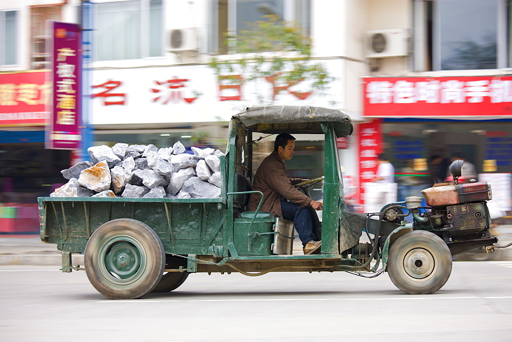 Man drives delivery tractor containing pile of construction stones in Yangshuo street, China