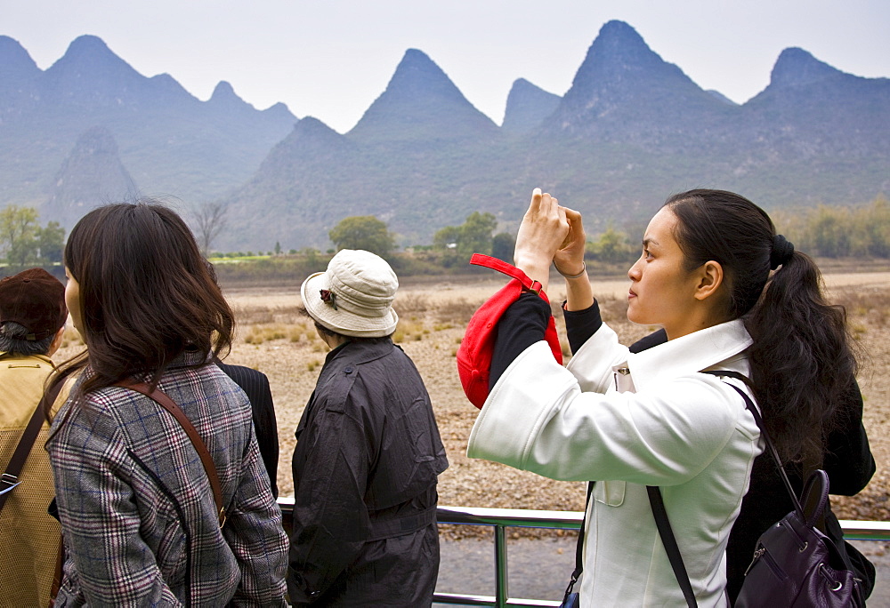 Tourist take photographs as she travels by boat along Li River between Guilin and Yangshuo, China