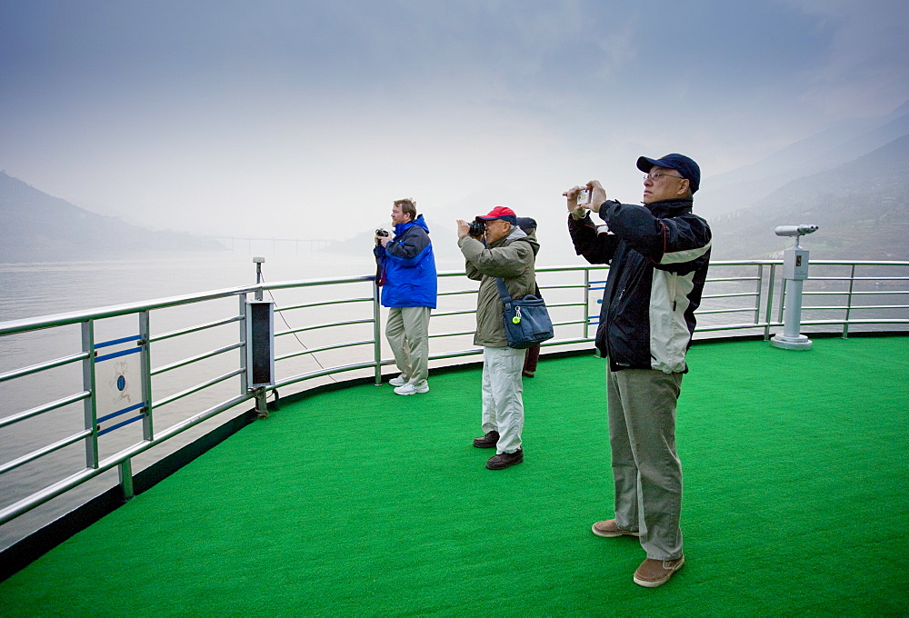 Tourists take photographs from the deck of a Victoria Line Cruise Ship, Yangze River, China