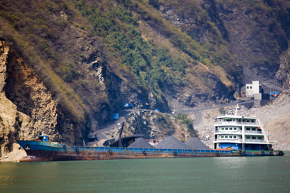 Freight ship being loaded with coal from delivery trucks on the shore, in Three Gorges area, Yangtze River, China