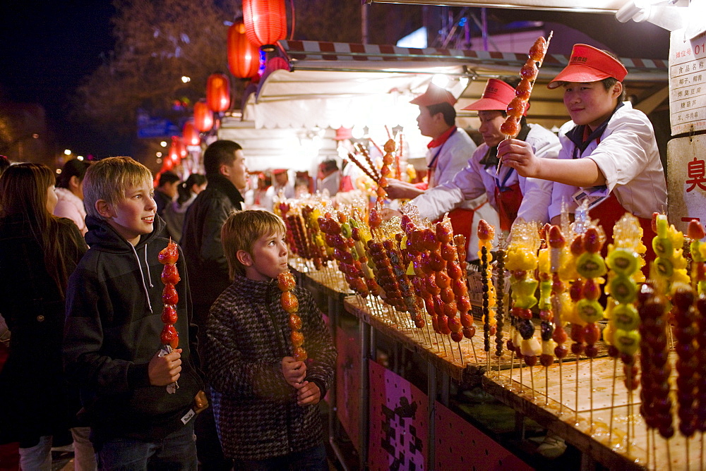 Boys eat candied strawberry sticks from stall in the Night Market, Wangfujing Street, Beijing, China