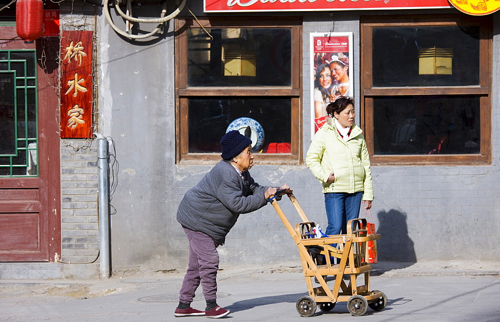 Elderly woman pushes wooden shopping cart along the pavement in the Hutongs area, Beijing, China