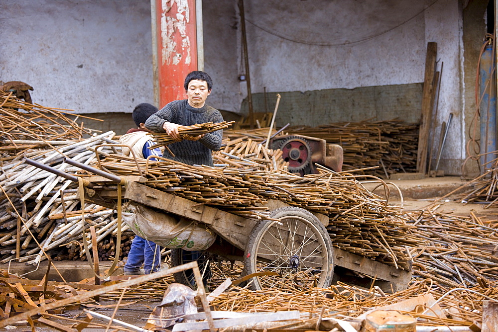 Man and boy working at metal recycling steel, loading a wooden cart, in Dazu County, Chongqing, China