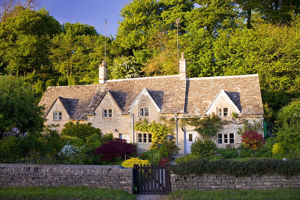 Terrace of traditional Cotswolds stone cottages with front gardens in  Bibury, The Cotswolds, Gloucestershire, UK