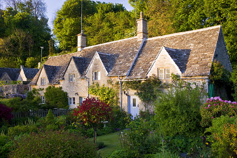 Terrace of traditional Cotswolds stone cottages with front gardens in  Bibury, The Cotswolds, Gloucestershire, UK