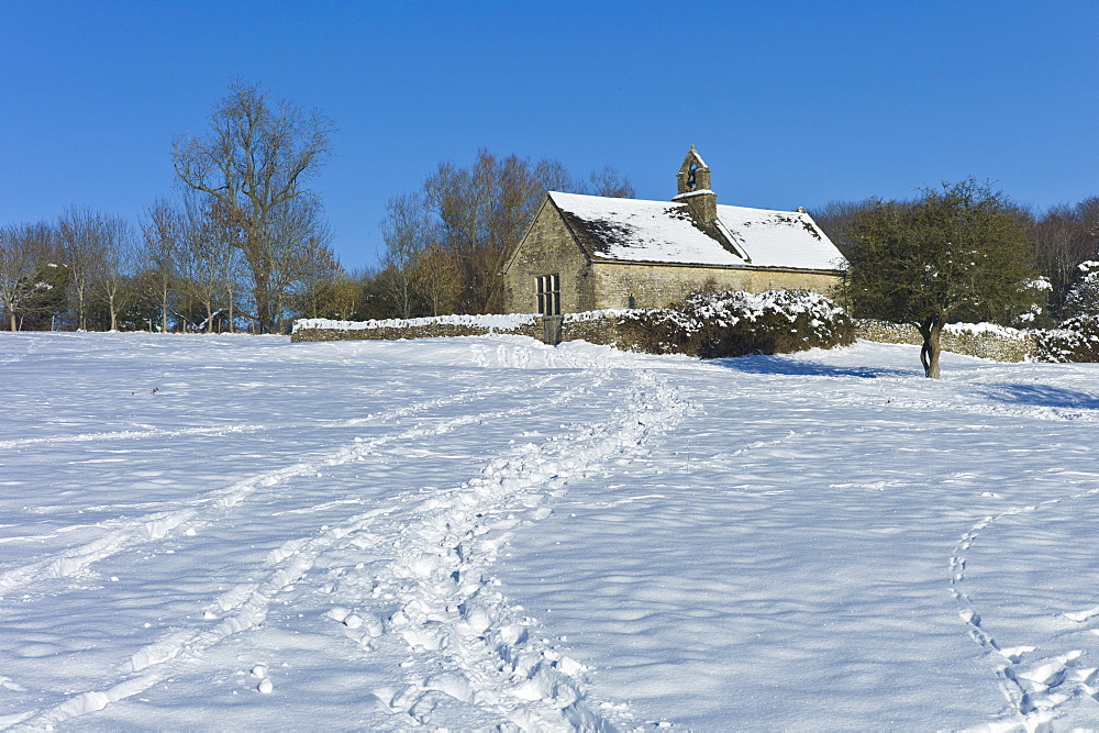 Quaint 13th Century chapel in snow-covered Windrush valley at Widford, The Cotswolds, UK