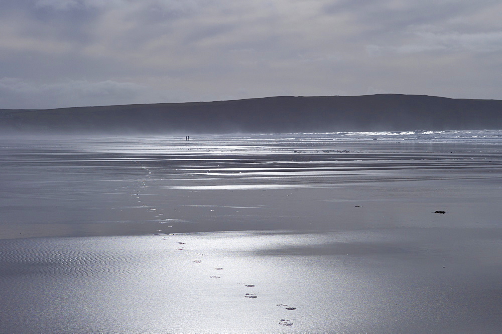 Couple walking on the beach leave footprints in the sand at Woolacombe, North Devon, UK