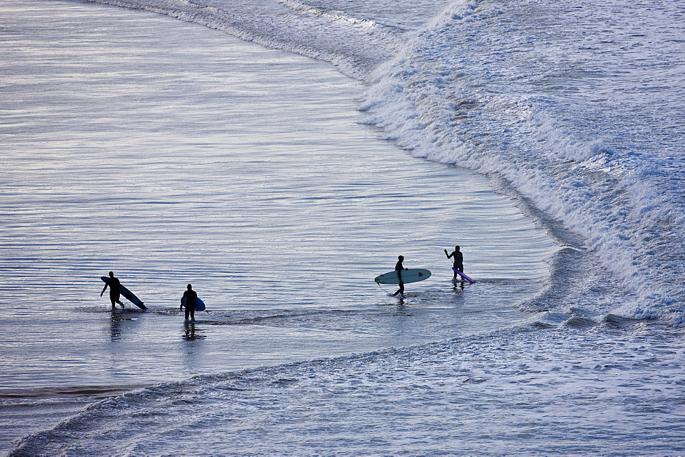 Surfers with surf boards approach waves breaking onto the beach at Woolacombe, North Devon, UK