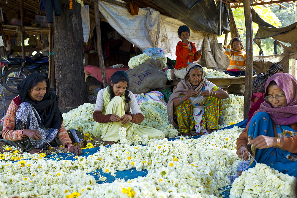 Indian women and children at work stringing garlands at Mehrauli Flower Market, New Delhi, India