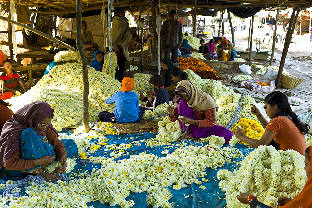 Indian women and children at work stringing garlands at Mehrauli Flower Market, New Delhi, India