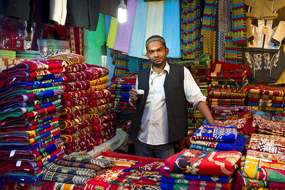 Stallholder drinking chai in shop selling prayer mats at muslim Meena Bazar, in Old Delhi, India