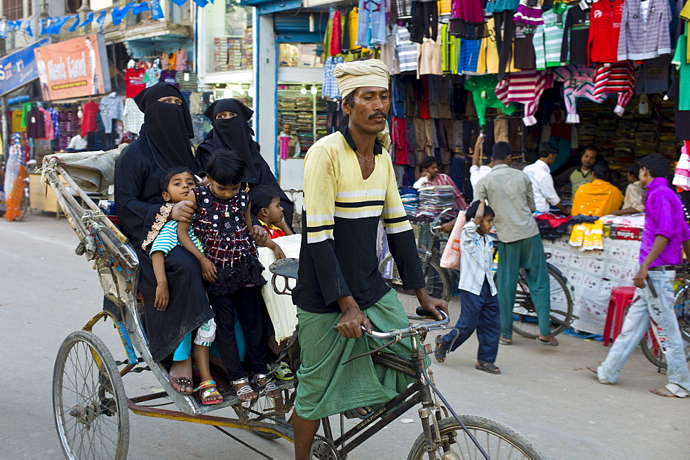 Street scene in holy city of Varanasi, young muslim women in black burkhas ride with their children in rickshaw, Benares, Northern India