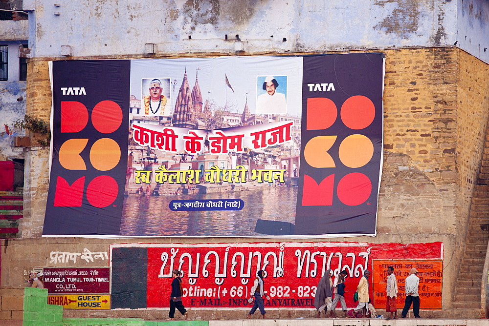 Indian people walking past TATA Docomo posters by the Ganges in holy city of Varanasi, Benares, Northern India