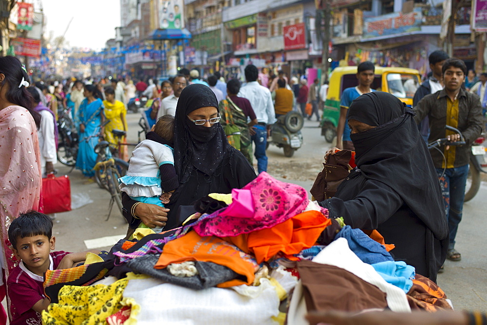 Street scene in holy city of Varanasi, young muslim women in black burkhas shopping with their children, Benares, Northern India