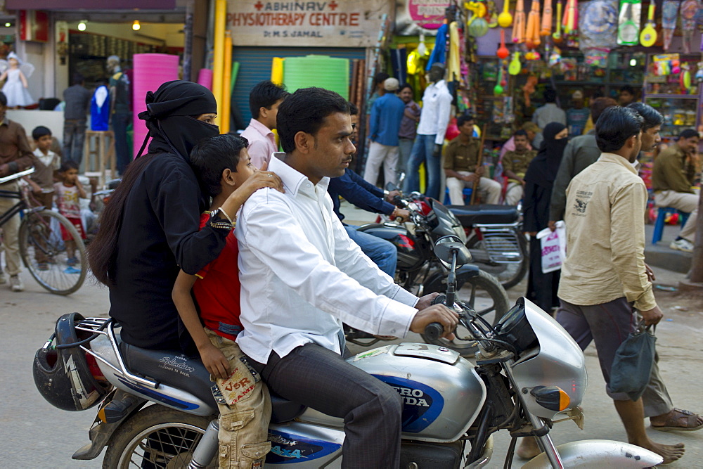 Young Indian Muslim family ride motorcycle in street scene in city of Varanasi, Benares, Northern India