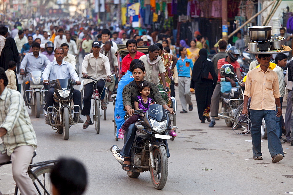 Fathers with children on cycles in crowded street scene during holy Festival of Shivaratri in city of Varanasi, Benares, Northern India