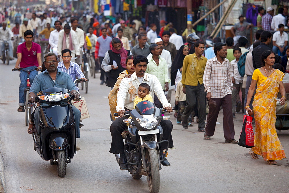 Fathers with children on cycles in crowded street scene during holy Festival of Shivaratri in city of Varanasi, Benares, Northern India