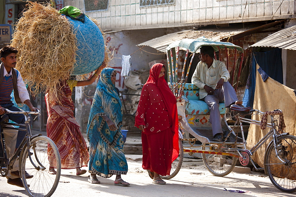 Indian women walking in the street, one carrying straw bale on head, in Nandi near Varanasi, Benares, Northern India