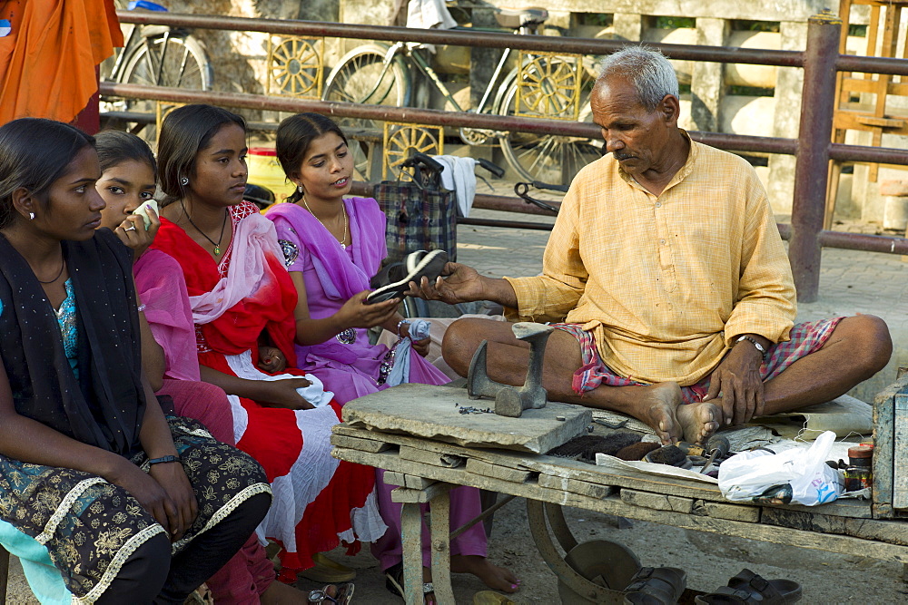 Indian girls in shoe shop with cobbler at work at Sarnath near Varanasi, Benares, Northern India