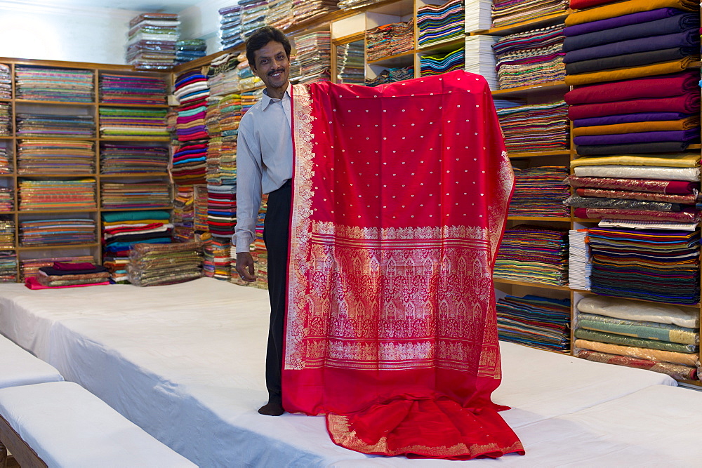 Indian man displays sari fabric at silk factory at Bressler near Varanasi, Benares, Northern India