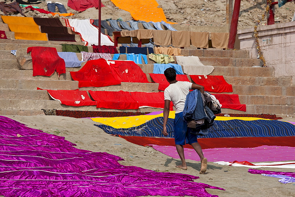 Indian man doing laundry using the waters of The Ganges River at Kali Ghat in City of Varanasi, Benares, India