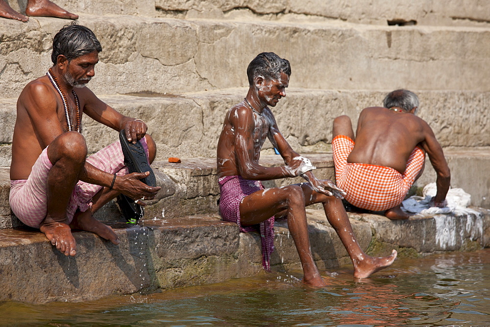 Indian men washing themselves and their clothes in waters of The Ganges River at Kali Ghat in City of Varanasi, Benares, India