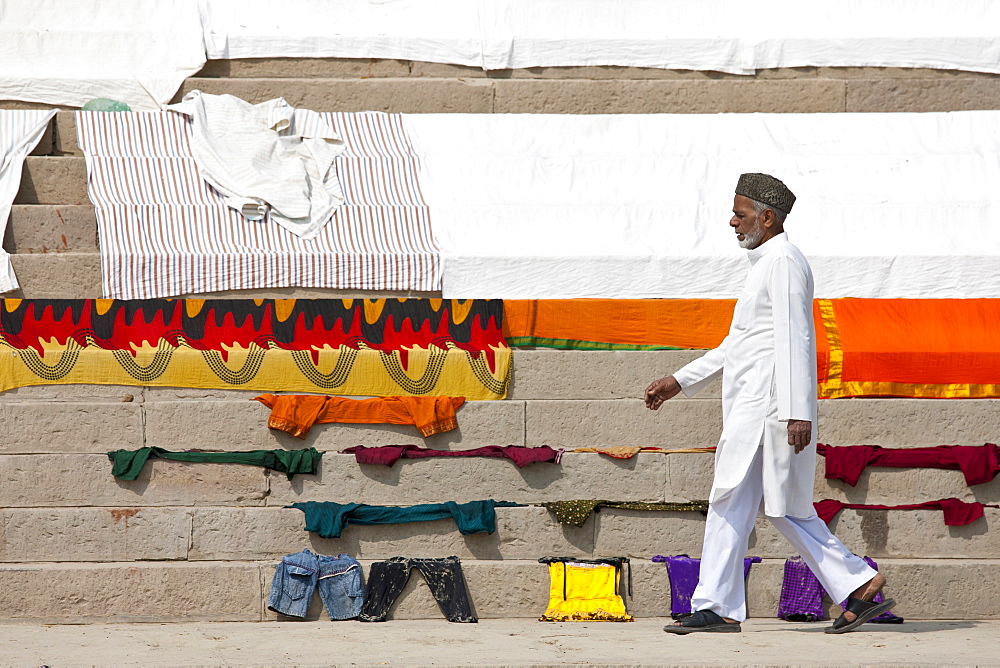 Indian man walks past laundry drying on the steps of Kali Ghat by the The Ganges River in City of Varanasi, Benares, India