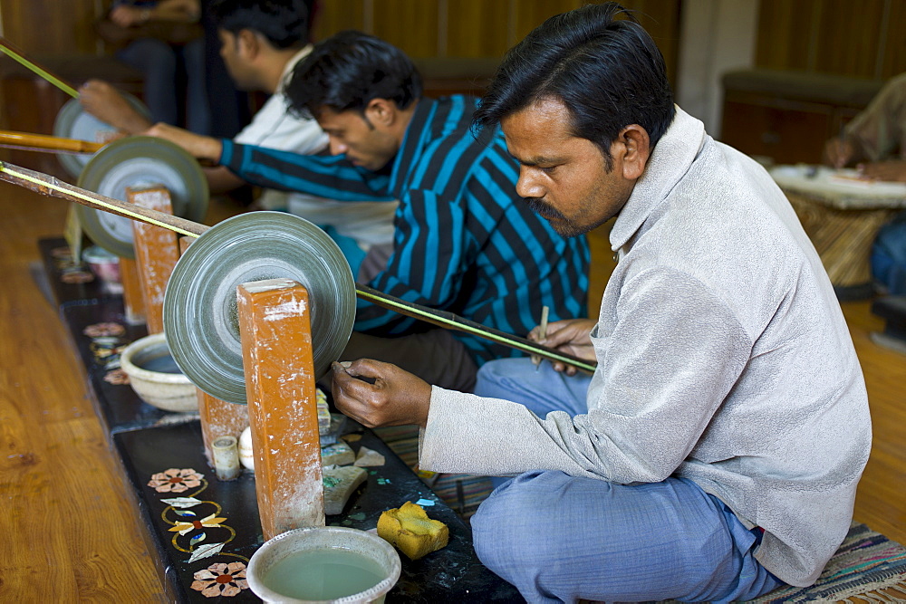 Skilled craftsmen at work making Pietra Dura souvenirs using traditional old-fashioned grinding wheel in Agra, India