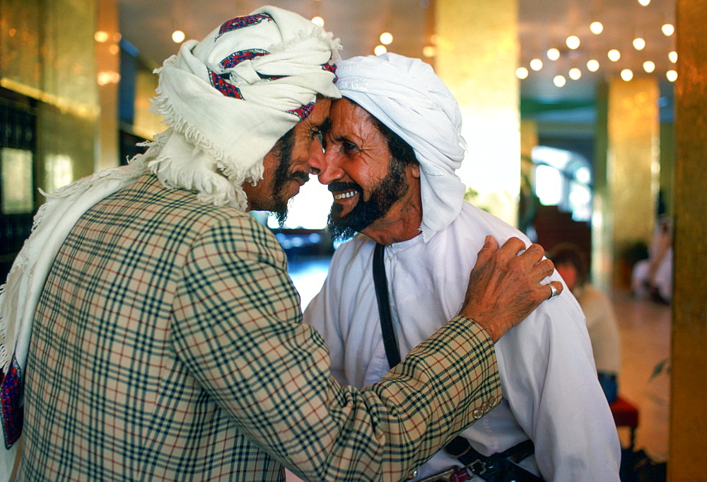 Two men wearing arab headdresses giving the traditional arab greeting in the Hilton Hotel at Al Ain, Abu Dhabi, United Arab Emirates