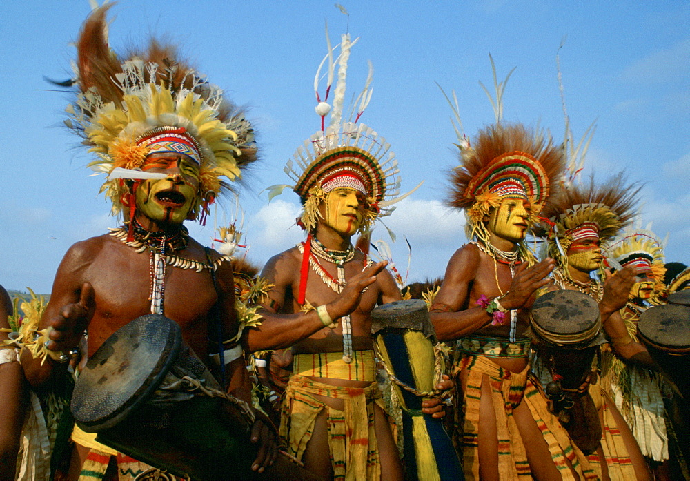 Tribesman musicians wearing war paints, feathered headdresses and necklaces made of bones and teeth playing drums and chanting during  a gathering of tribes at Mount Hagen in Papua New Guinea