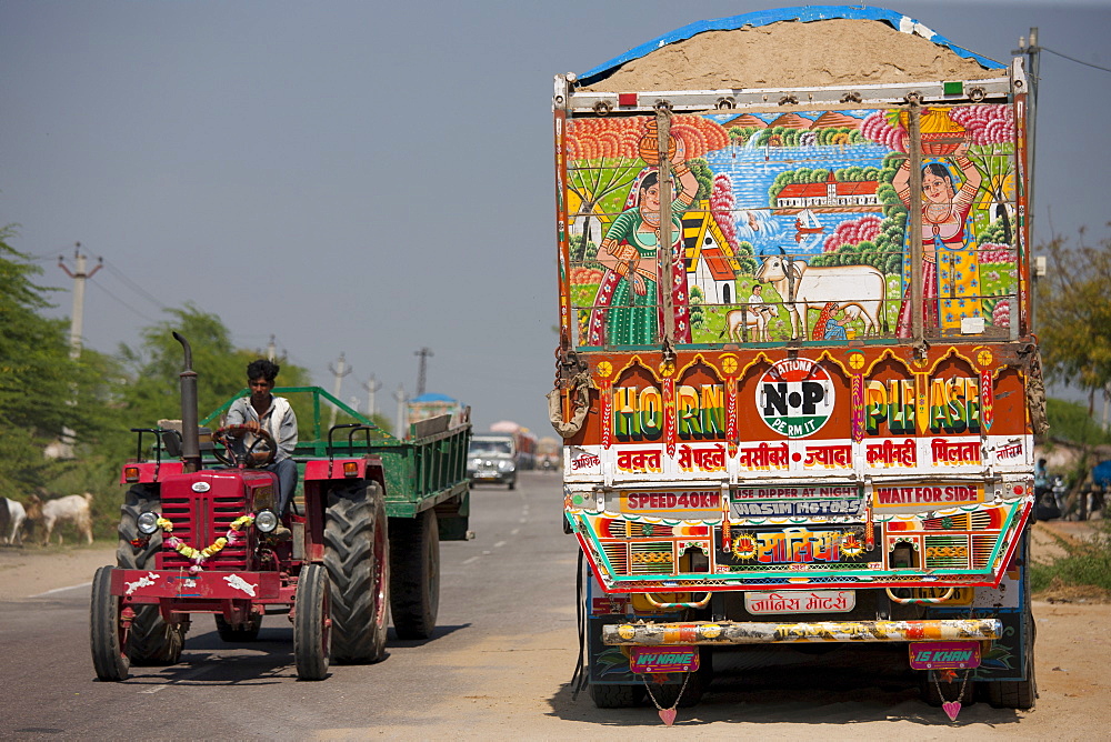 Indian farmer drives tractor past Tata trucks at Rasulpura in Sawai Madhopur, Rajasthan, Northern India