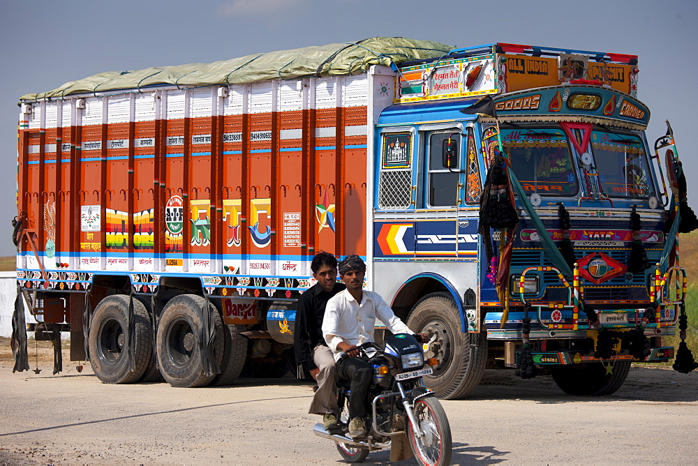 Indian motorcyclist rides past Tata trucks at Rasulpura in Sawai Madhopur, Rajasthan, Northern India