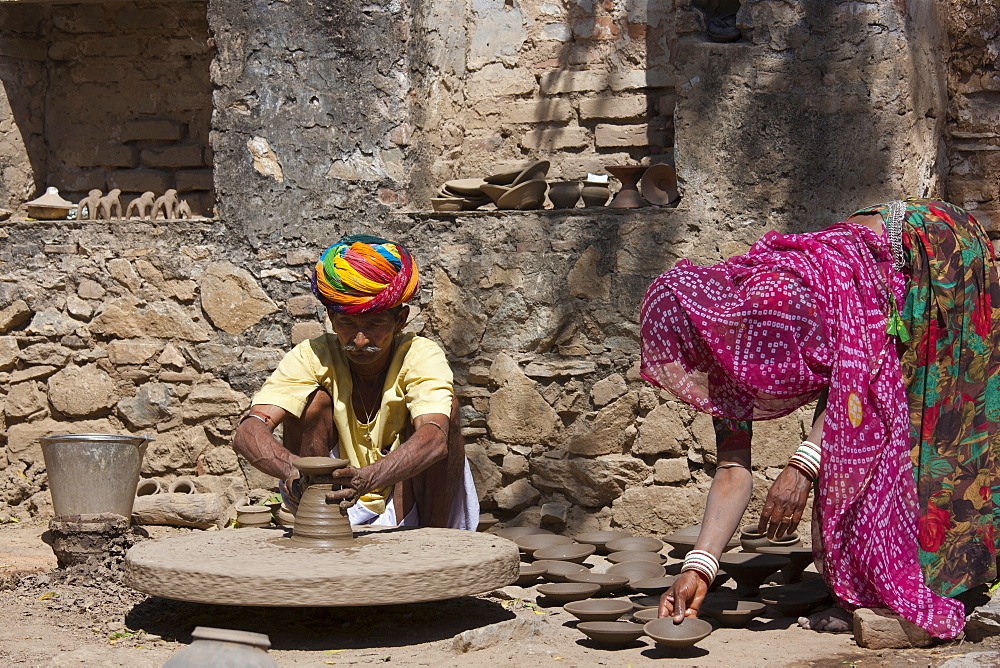 Indian potter in traditional Rajasthani turban works at home with his wife making clay pots in village of Nimaj, Rajasthan, Northern India