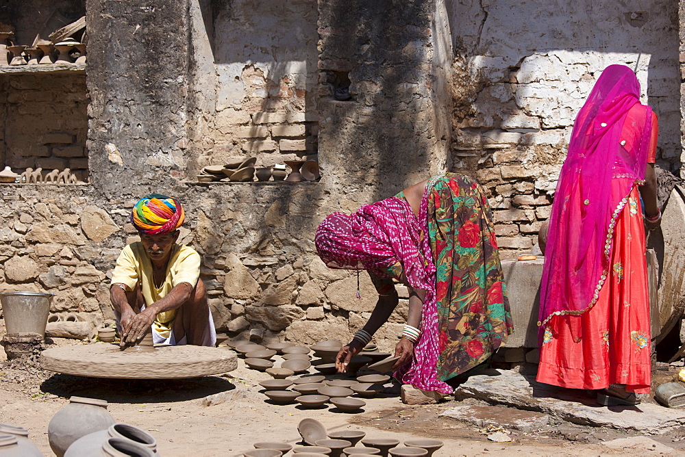 Indian potter in traditional Rajasthani turban works at home with his family making clay pots in village of Nimaj, Rajasthan, Northern India