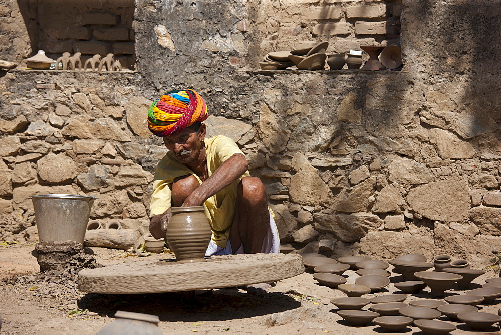 Indian potter in traditional Rajasthani turban works on potter's wheel at home making clay pots in Nimaj village, Rajasthan, Northern India