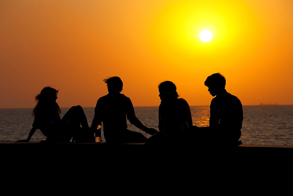 Young Indians sit on seawall at sunset at Nariman Point, Mumbai, formerly Bombay, India