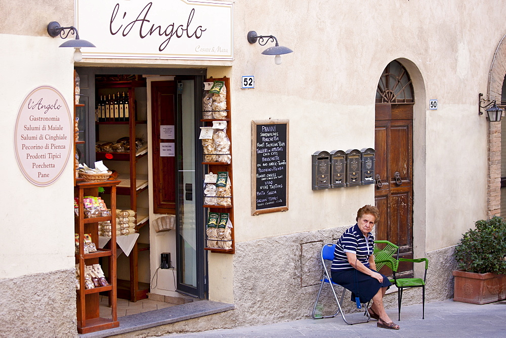 Local woman sitting outside L'Angolo delicatessen food shop in Montalcino, Val D'Orcia,Tuscany, Italy