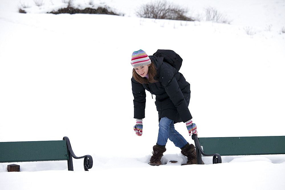 Young woman avoiding deep snow to reach park bench in snowy Tromso, Norway